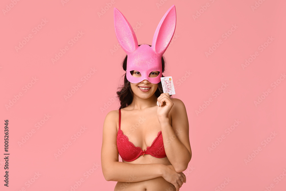 Beautiful young Asian woman in bunny mask and sexy lingerie with gift card on pink background Beautiful young Asian woman in bunny mask and sexy lingerie with gift card on pink background
