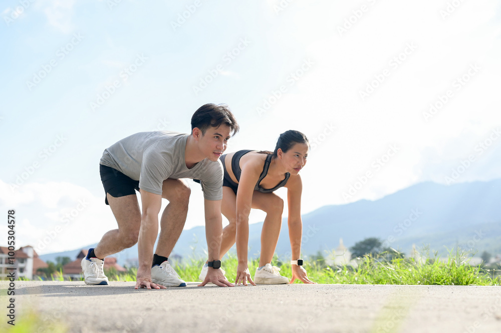 A confident, sporty Asian couple in sportswear is getting ready to sprint in the park.