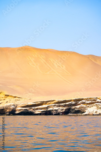 The famous Candelabra geoglyph etched into the sand dunes at Paracas Peninsula, Peru, under a clear blue sky. photo