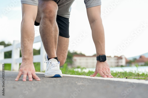 A cropped image of an active man in sportswear in a ready-to-run position, preparing to sprint.