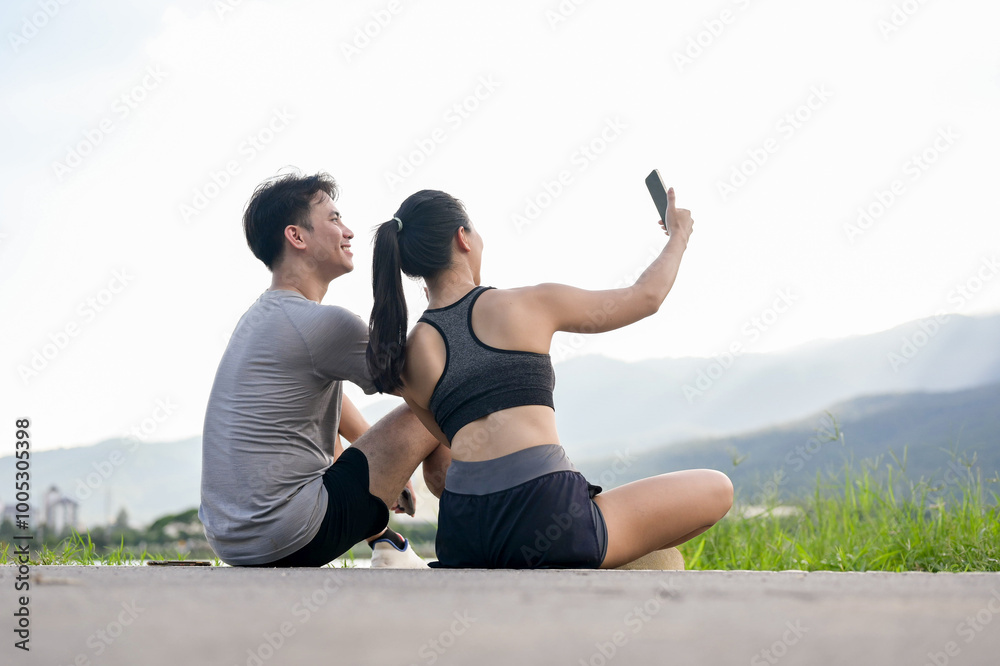 A lovely, sporty Asian couple is taking a selfie together while resting after their morning run. A lovely, sporty Asian couple is taking a selfie together while resting after their morning run.