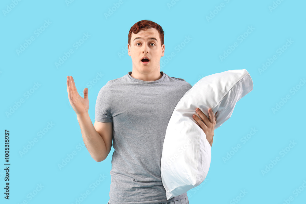 Handsome young shocked man in stylish pajamas with pillow on blue background Handsome young shocked man in stylish pajamas with pillow on blue background