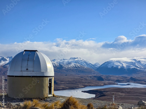 A unique dome-shaped observatory perched on a hillside with snow-capped mountains in the background. The clear, blue sky and distant peaks create a breathtaking backdrop for this scientific structure. photo