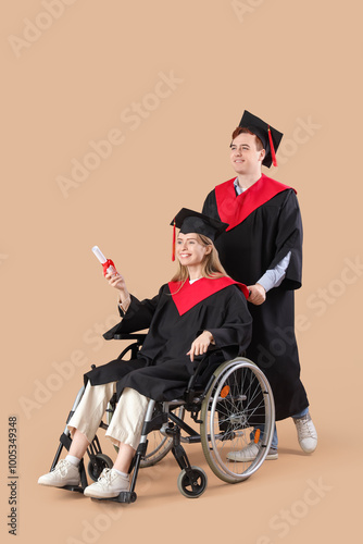 Male graduate in wheelchair with diploma and classmate on beige background