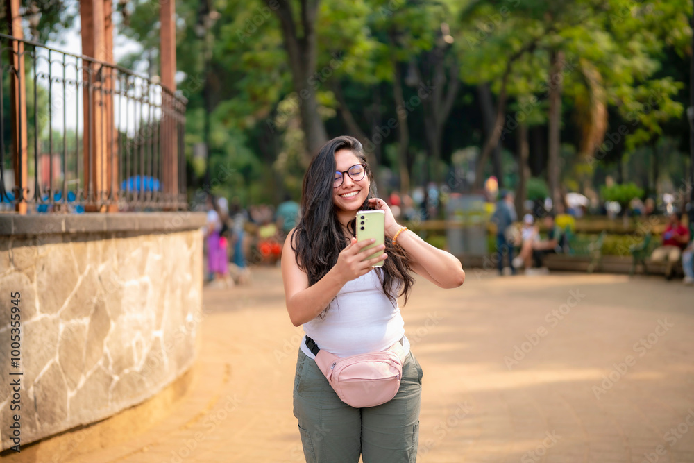 Young Latina woman taking a selfie and enjoying a sunny day in a park in Coyoacan, Mexico City, Mexico. Young Latina woman taking a selfie and enjoying a sunny day in a park in Coyoacan, Mexico City, Mexico.