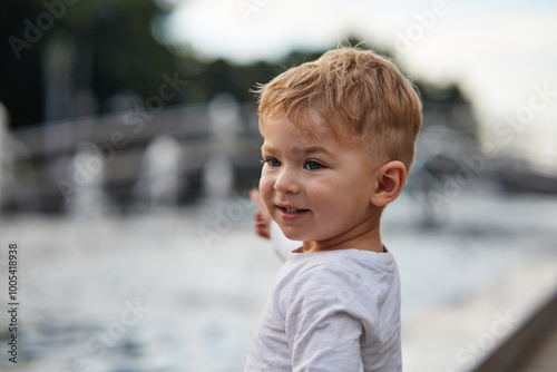 Close-up of a thoughtful young boy with light brown hair and blue eyes, looking off into the distance. The child is wearing a white t-shirt. Perfect for concepts of curiosity, childhood, innocence.