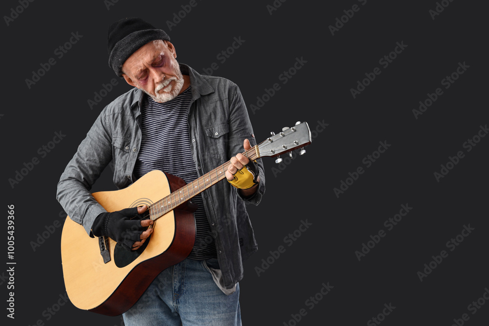 Mature homeless man playing guitar on dark background Mature homeless man playing guitar on dark background