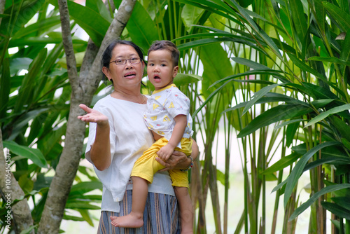 Grandma carrying her two-year-old grandson playing in the shade of the back garden photo