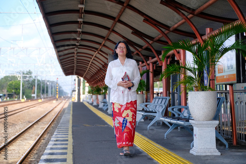 Woman wearing Javanese traditional dress, called Kebaya walking along a train station platform photo