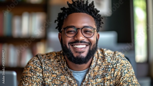 Smiling man sitting in a cozy environment with books in the background.