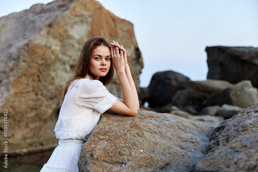 Naklejka premium serene young woman in white dress enjoys peaceful moment on rocky ocean shore