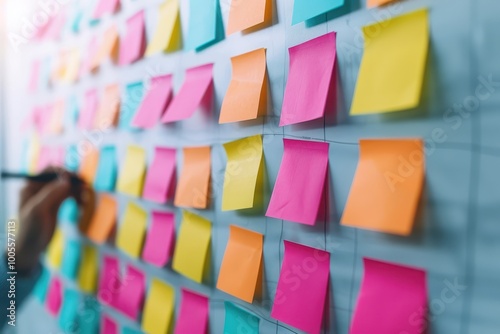 Brightly colored sticky notes in various shades, including pink, orange, and yellow, are arranged on a wall, being used for brainstorming and organization.