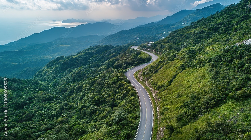 Fototapeta premium Breathtaking Mountain Landscape from Above: A Wide Road Winding Upward Through Lush Greenery and Rocky Terrain. This Scenic View Captures the Majesty of Nature, Showcasing Rolling Hills, Clear Skies, 