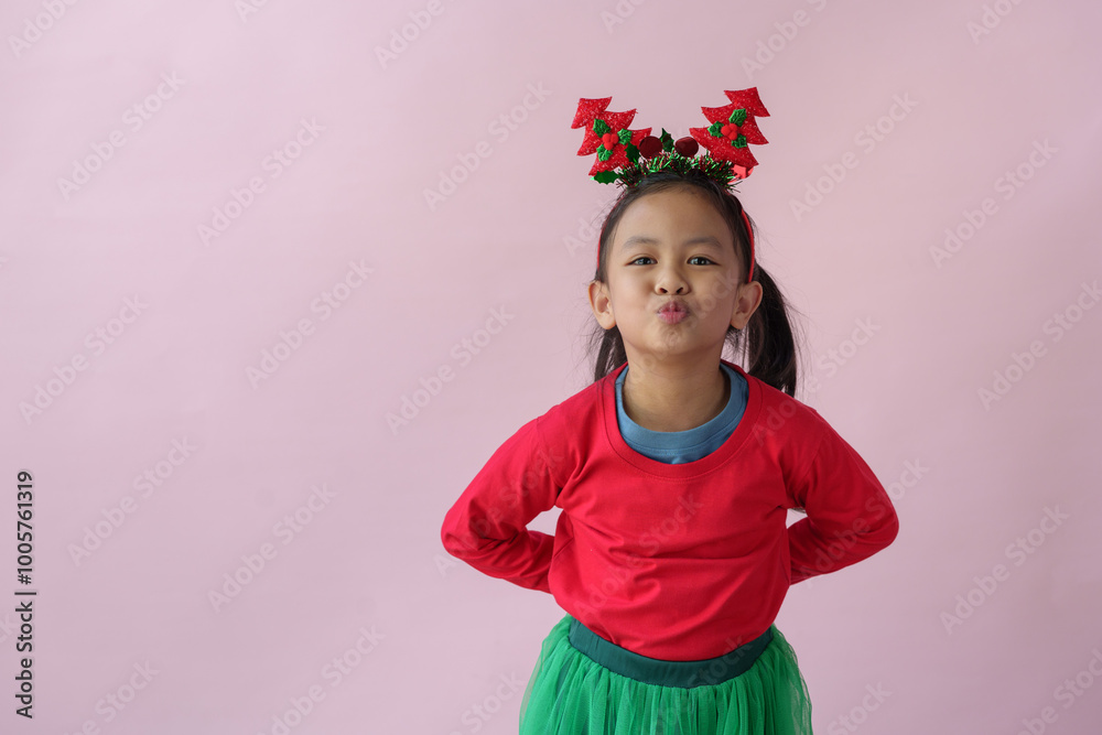 Adorable little Asian girl with Christmas tree headband, antlers showing various poses, standing, smiling, laughing, having fun in various poses, pink background. Holiday concept annual festival.