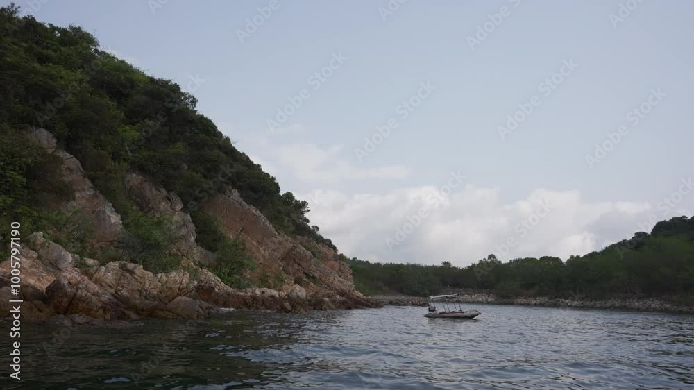 A small empty boat anchored in the sea near by the shore and beautiful rocks in a sunny day