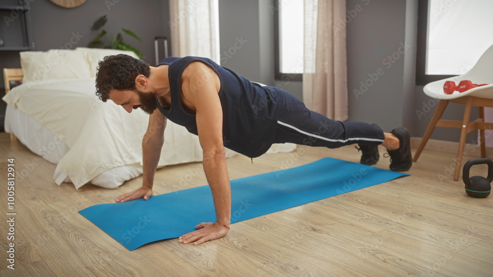 Muscular man doing pushups on a blue mat in a modern bedroom, showcasing fitness and a healthy lifestyle at home.