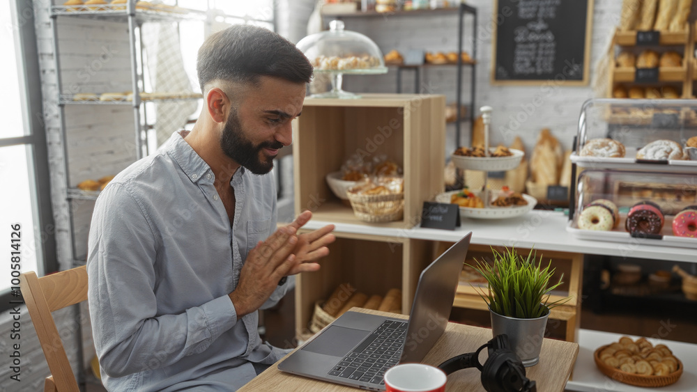 Young hispanic man working on laptop in a cozy bakery interior filled with assorted pastries and desserts Young hispanic man working on laptop in a cozy bakery interior filled with assorted pastries and desserts