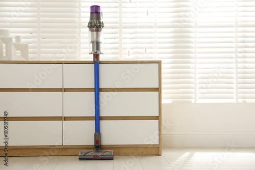Photos One cordless vacuum cleaner leaning on chest of drawers indoors