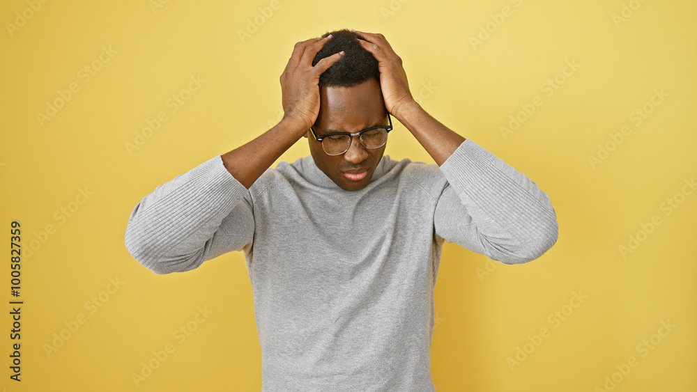 Stressed young man in glasses against yellow background clutching his head Stressed young man in glasses against yellow background clutching his head