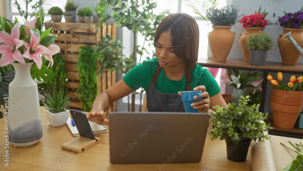 A focused woman uses a laptop and mobile phone in an indoor flower shop surrounded by vibrant plants. A focused woman uses a laptop and mobile phone in an indoor flower shop surrounded by vibrant plants.