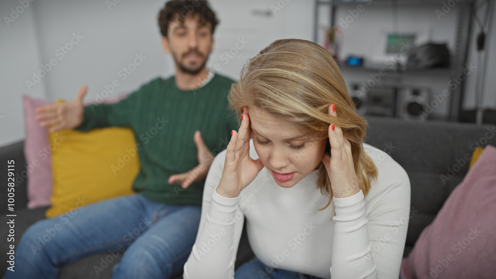 Fototapeta premium A distressed woman with a man gesturing in a blurry background, illustrating conflict in a modern living room setting.