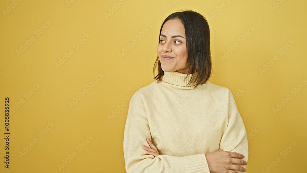 Confident hispanic woman in a cream sweater poses with arms crossed against a yellow background, symbolizing positivity. Confident hispanic woman in a cream sweater poses with arms crossed against a yellow background, symbolizing positivity.