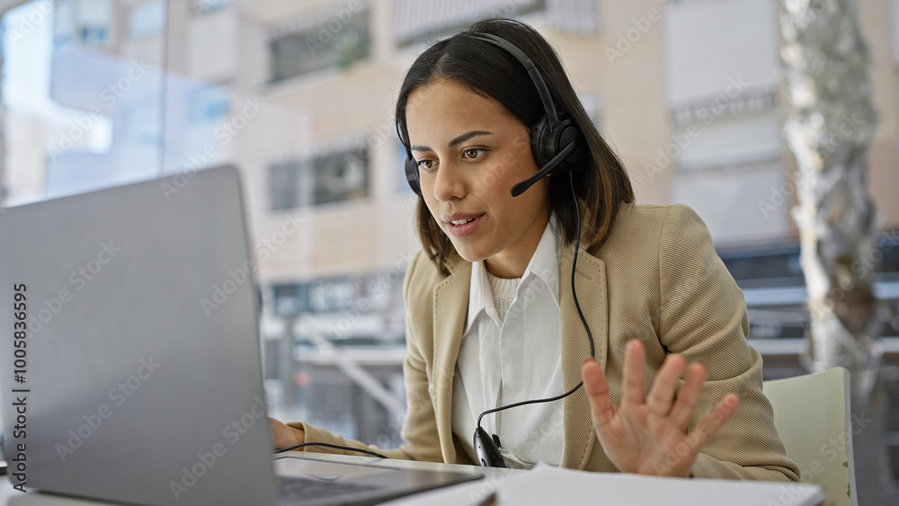 A professional hispanic woman with a headset communicates during a video call in a modern office. A professional hispanic woman with a headset communicates during a video call in a modern office.