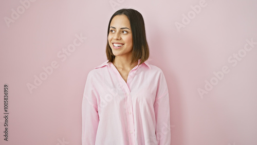 Portrait of a smiling young hispanic woman in a pink shirt against an isolated pink background.