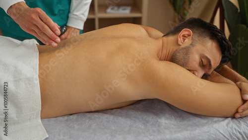 Man receiving relaxing massage therapy indoors at wellness spa center with masseur applying hot stone treatment on back