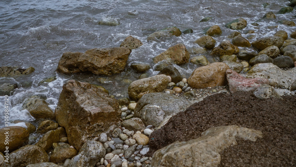 Rocky shoreline with various sizes of stones and pebbles scattered along the coastal edge, waves gently lapping against the rocks creating a rugged natural beach scene.