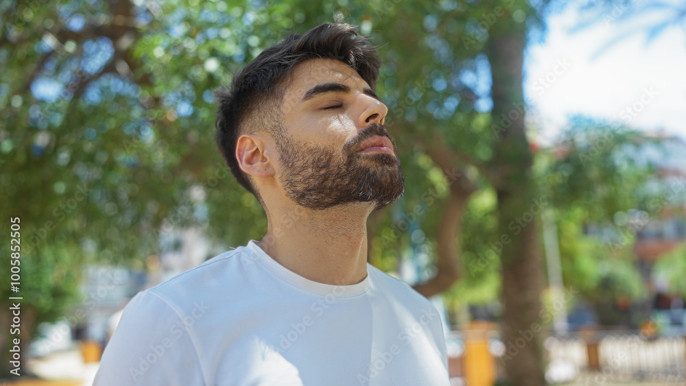 Handsome man with beard enjoying peaceful moment outdoors in urban park with eyes closed and sunlight filtering through trees Handsome man with beard enjoying peaceful moment outdoors in urban park with eyes closed and sunlight filtering through trees