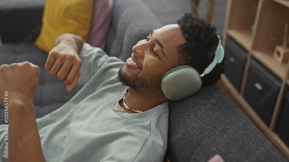 Smiling african american man lounging on a couch with headphones in a modern living room. Smiling african american man lounging on a couch with headphones in a modern living room.