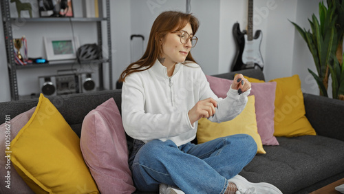 A casual young woman sits on a couch indoors, looking at her smartwatch in a modernly furnished living room. photo