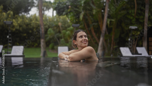 A young, happy woman relaxes in a bali resort's outdoor pool surrounded by tropical foliage.