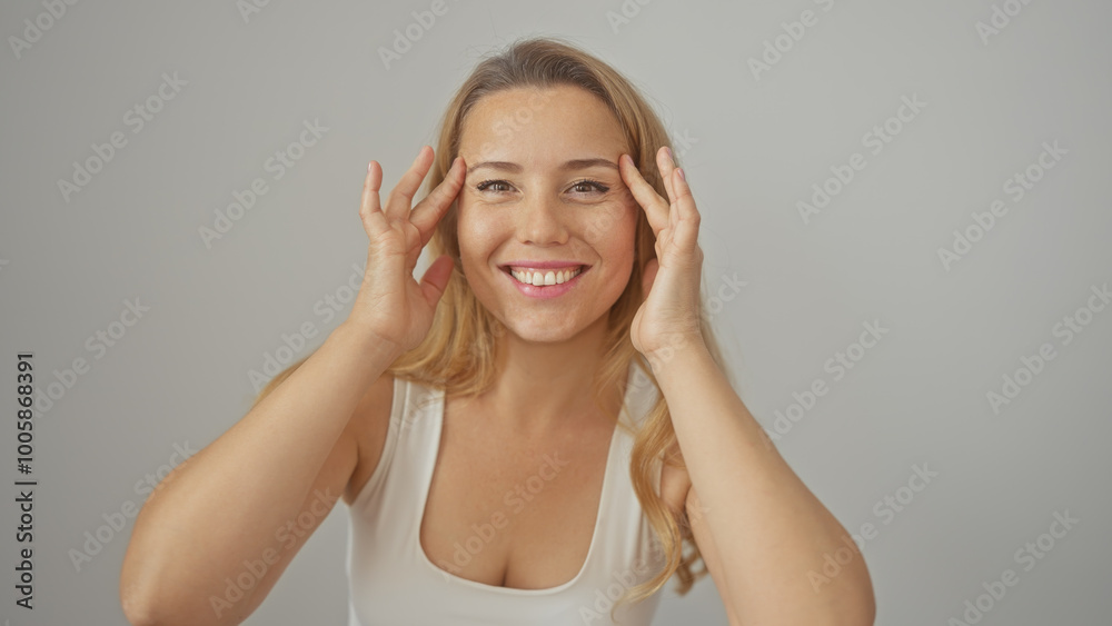 Smiling blonde woman touching face against a white isolated background, exuding happiness and confidence. Smiling blonde woman touching face against a white isolated background, exuding happiness and confidence.