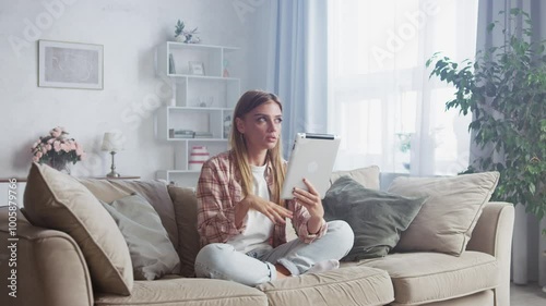 Wallpaper Mural Young woman is sitting on a comfortable sofa in her living room, using a tablet. She is making gestures while looking at the screen Torontodigital.ca