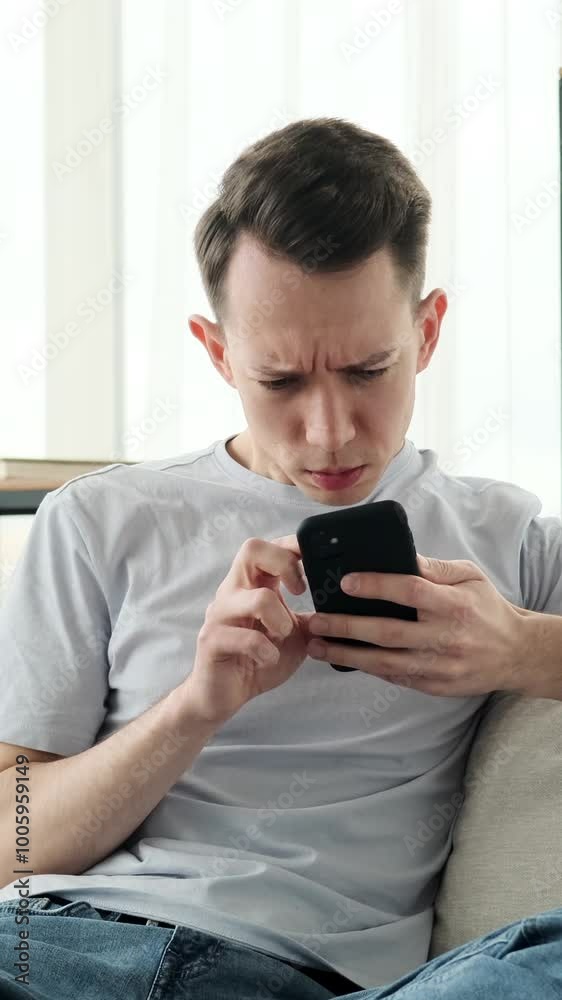 Surprised Caucasian man messaging in internet social media with cellphone and exclaiming wow, receiving good news at home. Vertical video. Surprised Caucasian man messaging in internet social media with cellphone and exclaiming wow, receiving good news at home. Vertical video.