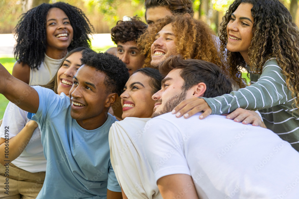 A multiculltural group of friends huddles closely together, smiling and taking a selfie at an outdoor gathering.