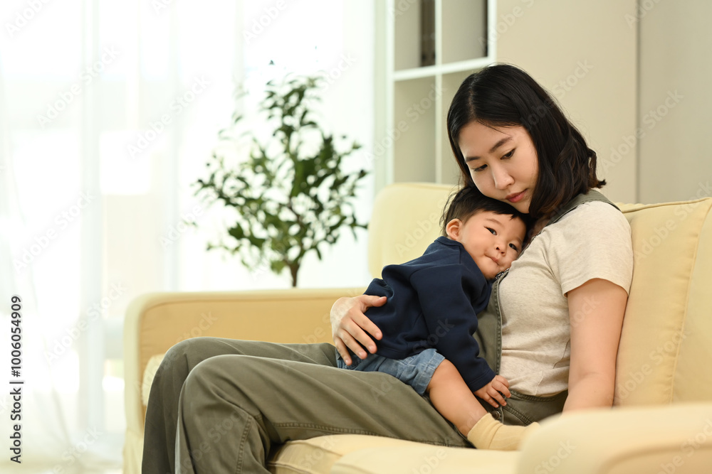 Loving asian mother with her cute little toddler boy sitting on comfortable couch at home Loving asian mother with her cute little toddler boy sitting on comfortable couch at home