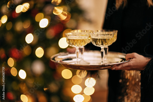 Close-up of a young woman hands holding a beautiful metal tray with four glasses of champagne. A New Year dinner with alcohol drinks. A festive meeting of friends. photo