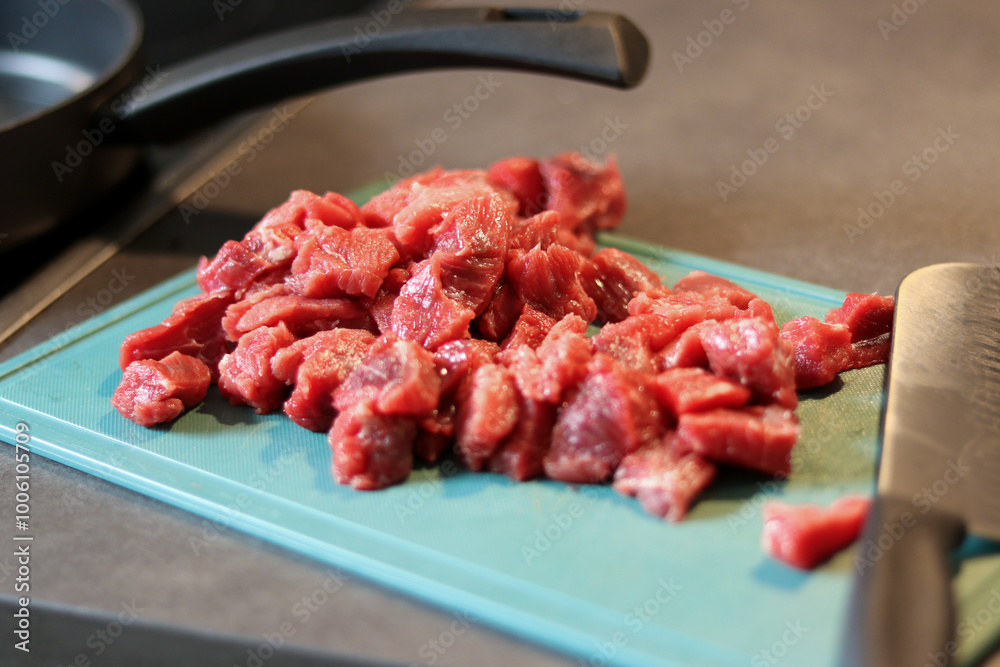Close up of raw beef meat chopped in small cubes on green cutting board with a knife Close up of raw beef meat chopped in small cubes on green cutting board with a knife