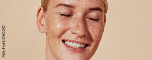 Close up highly detailed studio shot of a young female with freckles. Portrait of a smiling woman with blond hair and smooth skin against a beige background.