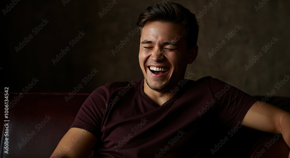 Smiling young man laughing on a leather couch. Indoor portrait with dark background Smiling young man laughing on a leather couch. Indoor portrait with dark background