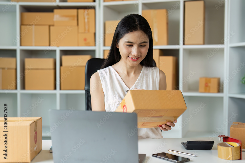 Young Entrepreneur Working on Small Business Packaging Orders in Home Office with Laptop and Smartphone Young Entrepreneur Working on Small Business Packaging Orders in Home Office with Laptop and Smartphone