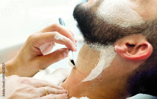 Barber shaving customer with straight razor in barbershop photo