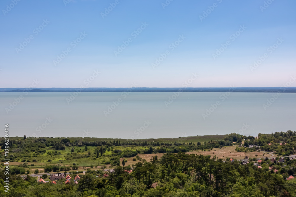 Obraz premium Panoramic aerial view of Balaton lake seen from observation tower Padkui Kilato in Balatongyorok, Hungary, Europe. Small villages along the lakeshore surrounded by rolling hills and lush greenery