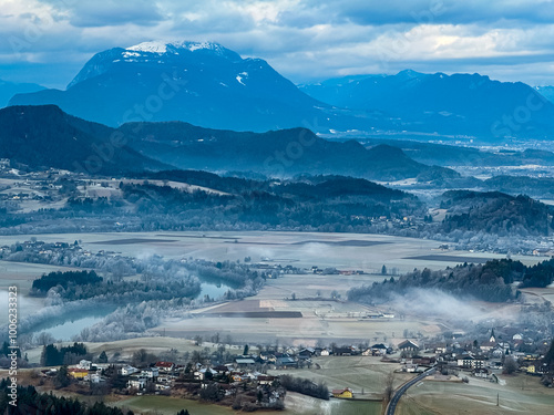 Aerial scenic view of dreamy Rosental valley and majestic snow-capped mountain peak Dobratsch, Carinthia, Austria. Fog covered tranquil alpine landscape. Peaceful scene in Austrian Alps in winter photo