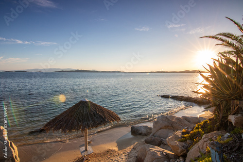 View through rocks on a sandy beach into the sunset. Landscape shot with a view to the horizon over the wide sea on the coast of Ouranoupoli, Thessaloniki, Central Macedonia, Greece photo