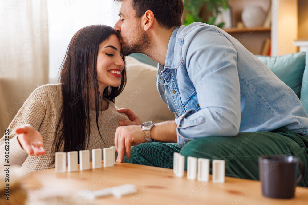 Fototapeta premium Man kissing woman in forehead while playing dominoes at home