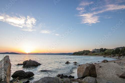 View through rocks on a sandy beach into the sunset. Landscape shot with a view to the horizon over the wide sea on the coast of Ouranoupoli, Thessaloniki, Central Macedonia, Greece photo